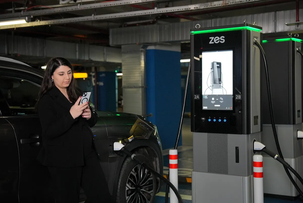 A driver using the Zes app on their phone beside a Zes station